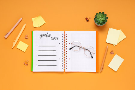 Notebook with 2026 goals, eyeglasses and stationery on orange backgroundの写真素材