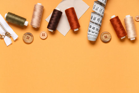 Different thread spools with buttons, measuring tape and zipper on orange background