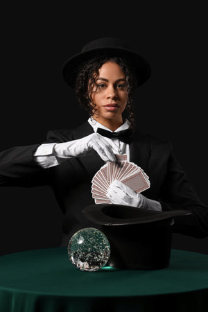 Young African-American magician with cards and crystal ball on table against black backgroundの写真素材