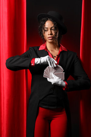 Young magician with cards near red curtains on dark backgroundの写真素材
