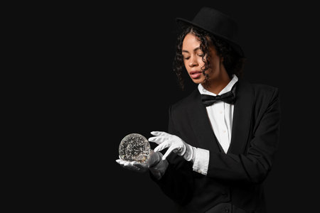 Young African-American magician with crystal ball on black backgroundの写真素材
