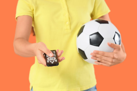 Young woman with TV remote controller watching football on orange background, closeupの写真素材