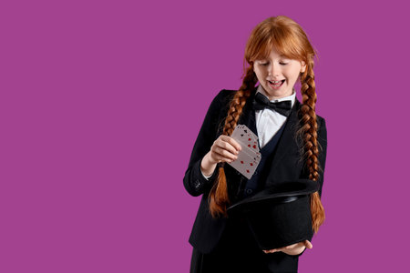 Young magician showing magic trick with playing cards and hat on purple backgroundの写真素材