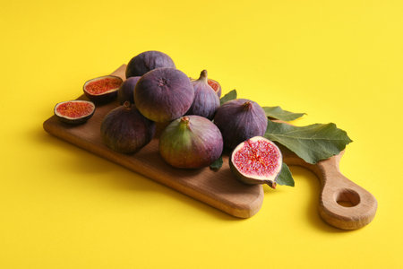 Wooden board with fresh ripe figs on yellow background
