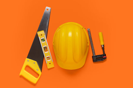 Yellow hardhat with handsaw, spirit level and clamp on orange backgroundの写真素材