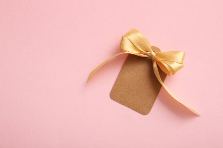 Blank paper tag with bow made of golden ribbon on pink backgroundの写真素材