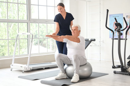 Senior man training with therapist on fitball in rehabilitation center