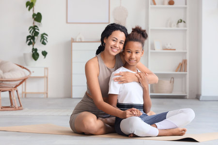 Teenage African-American girl with her mother hugging on yoga mat at homeの写真素材