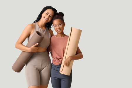 African-American mother with her teenage daughter and yoga mats hugging on light backgroundの写真素材