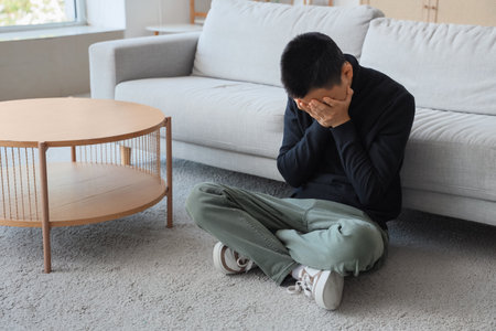 Sad young Asian man sitting on carpet at homeの写真素材