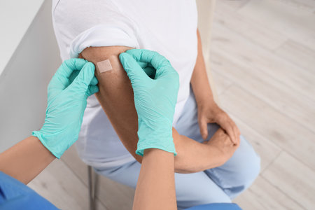 Female doctor applying medical patch onto senior woman's arm after vaccination in clinic, closeupの写真素材