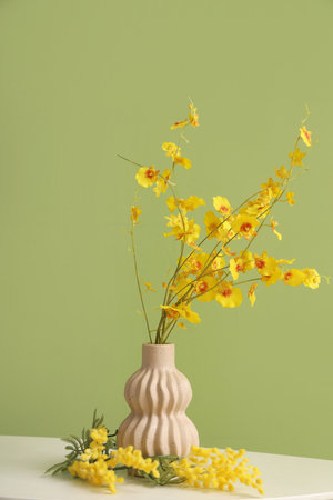 Vase with yellow flowers on table against green backgroundの写真素材