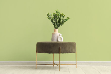 Vase with artificial plant on pouf near green wall