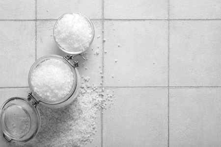 Glass jar and bowl with sea salt on light tile background