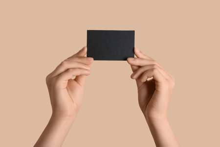 Female hands with blank black business card on beige backgroundの写真素材
