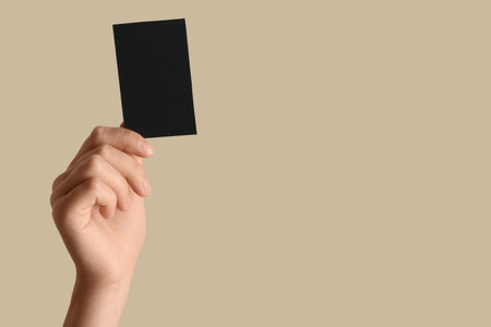 Female hand with blank black business card on beige backgroundの写真素材