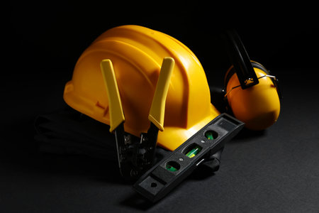 Hardhat, construction tools and protective earmuffs on black background, closeup
