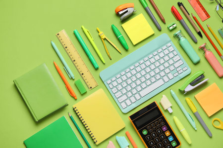 Composition with modern computer keyboard and different stationery on green background