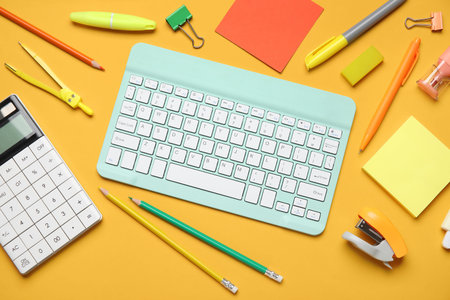 Composition with modern computer keyboard and different stationery on orange background