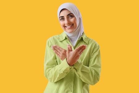Beautiful Muslim woman using sign language on yellow backgroundの写真素材