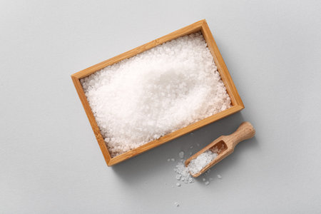 Wooden box with sea salt and scoop on light backgroundの写真素材