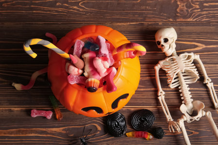 Decorative pumpkin with different sweet candies and skeleton on wooden background. Halloween celebrationの写真素材