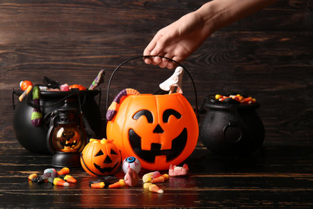 Female hand with decorative pumpkins and cauldrons of different sweet candies on black wooden table. Halloween celebrationの写真素材