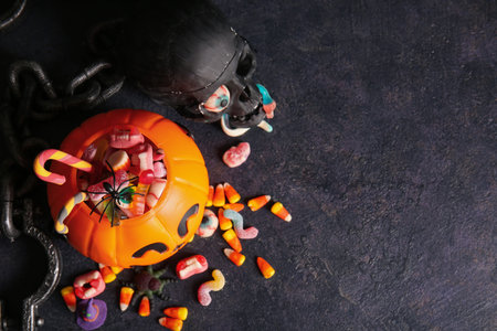 Decorative pumpkin with different sweet candies and skull on dark background. Halloween celebration