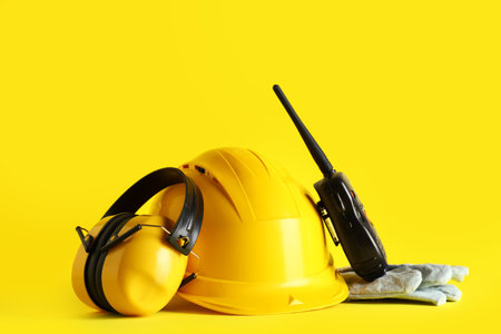 Hardhat, protective earmuffs and radio transceiver on yellow backgroundの写真素材