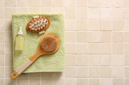 Composition with clean towel, bottle of cosmetic product and massage body brushes on beige tile background, closeupの写真素材