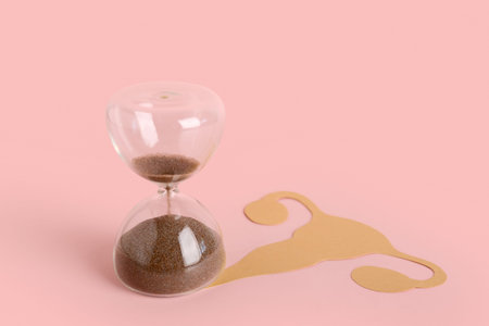 Hourglass with paper uterus on pink background. Gynecology conceptの写真素材