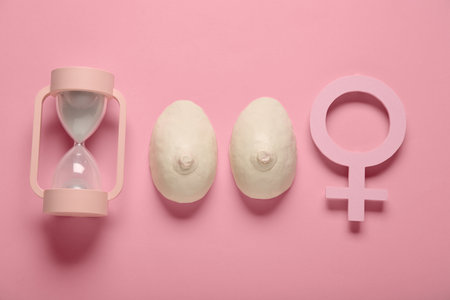 Hourglass with breast models and symbol of woman on pink background. Gynecology conceptの写真素材