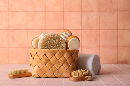 Composition with wicker basket and different massage body brushes on pink tile background, closeup