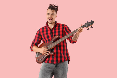 Young man playing electric guitar on pink background