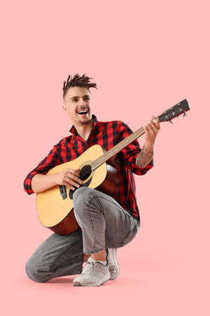 Young man playing guitar on pink backgroundの写真素材