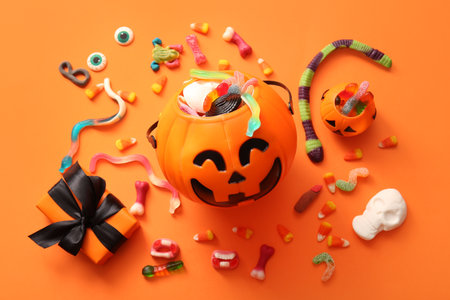 Cauldrons in shape of pumpkin with candies for Halloween and gift box on orange background, closeupの写真素材