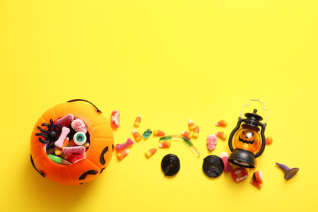 Cauldron with different candies for Halloween and lantern on yellow backgroundの写真素材