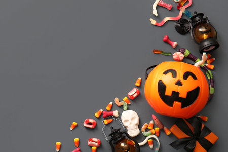 Composition with cauldron in shape of pumpkin, candies for Halloween, lanterns and gift box on gray backgroundの写真素材