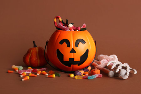 Cauldron in shape of pumpkin with candies for Halloween, skeleton hand and bones on brown background, closeupの写真素材