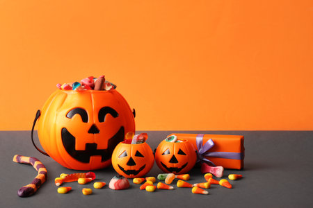 Cauldrons in shape of pumpkin with candies for Halloween and gift box on orange backgroundの写真素材