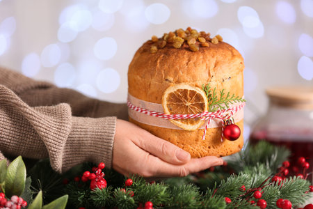 Female hands with Panettone and Christmas wreath against blurred lights, closeup