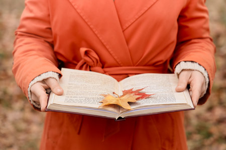 Woman with book and autumn leaf in park, closeupの写真素材