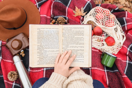 Woman reading book on plaid in autumn park, top view