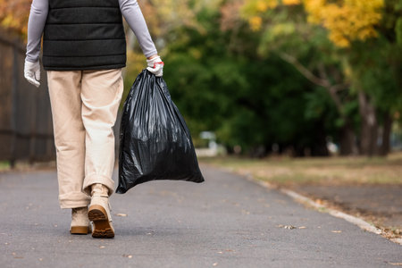 Woman with garbage bag walking on street, back view