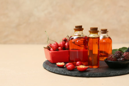 Bottles of cosmetic rose hip oil and bowl with berries on beige backgroundの写真素材