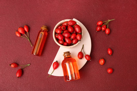 Bottles of cosmetic rose hip oil and bowl with berries on red backgroundの写真素材