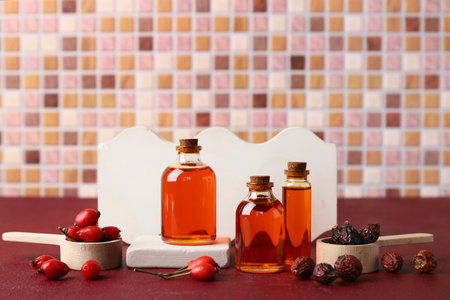 Decorative podiums with bottles of cosmetic rose hip oil and berries on red tableの写真素材