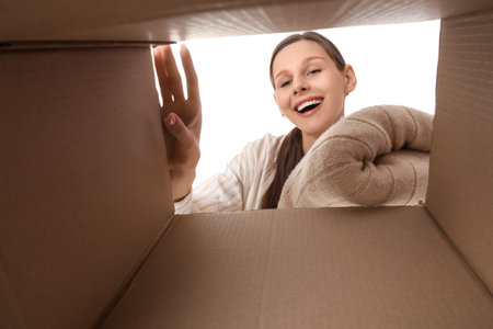 Young woman taking clothes from open moving box on white background, view from inside