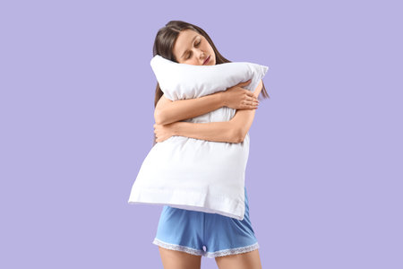 Female sleepwalker in pajamas with pillow on lilac backgroundの写真素材