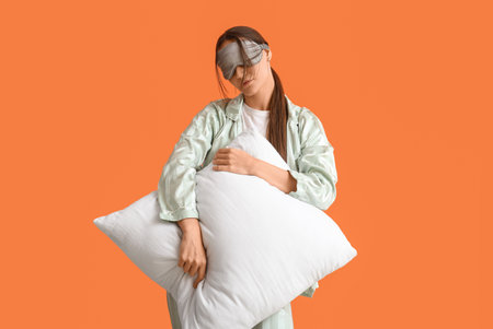 Female in pajamas with pillow on orange backgroundの写真素材